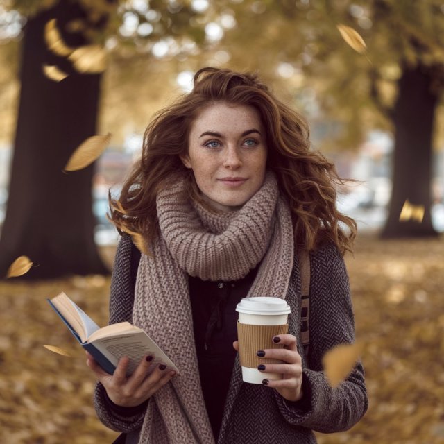 Young woman in a park in autumn holding a cup of coffee and a book